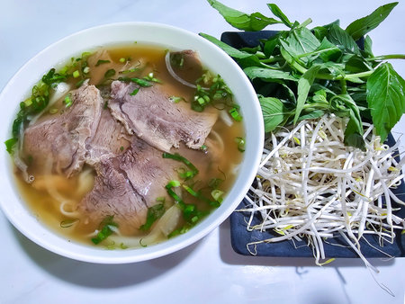 Top view of the famous Vietnamese Pho soup with sliced beef, fresh green mint and young bean...