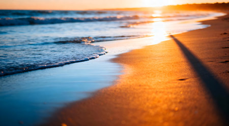 This image captures the serene beauty of a beach at sunset, featuring soft waves lapping against the shore. The scene is bathed in the warm hues of golden hour, with the sky transitioning from soothing blue to vibrant orange. The artistic composition enhances the natural tranquility, ideal for use in relaxation and wellness themes. AI-generated illustration.の素材