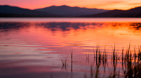 This image captures a tranquil lake during sunset, bathed in the soft glow of golden hour. The scene is dominated by vivid orange and subtle pink tones, creating a peaceful and serene atmosphere. Ideal for use in meditation guides, nature-themed decor, or as a calming backdrop for personal spaces. AI-generated illustration.の素材