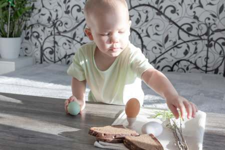 A little boy celebrates Easter, sits at a wooden table and eats