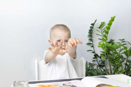A little boy paints with watercolor paints on a table next to a green flowerの写真素材