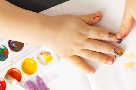 A little boy paints with watercolor paints on a tableの写真素材