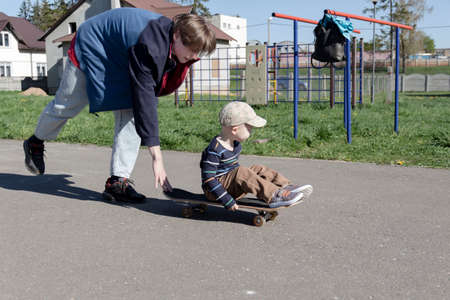 The older brother patiently and lovingly teaches the little boy his favorite - to skate on a playground hobby in the park in the fresh air.の写真素材