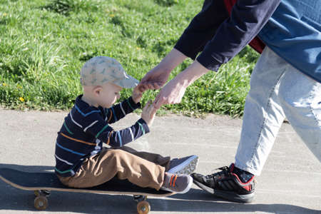 The older brother patiently and lovingly teaches the little boy his favorite - to skate on a playground hobby in the park in the fresh air.の写真素材