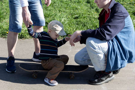 Dad teaches his young son of three years together with his eldest teenage son to ride a skateboard, in the fresh air, on a special area for skateboarders.の写真素材