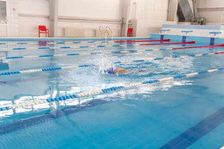 A male athlete swims in a swimming pool sports complex in blue waterの写真素材