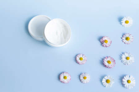 Fresh flowers, daisies are laid out in a corner and a white jar with a cream cosmetic on a blue background and a free space for advertising.の写真素材