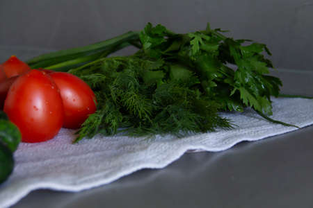 Fresh, delicious vegetables cucumbers, tomatoes and greens with dill and parsley lie on the kitchen, gray surface on a linen towel and are ready for cooking pasta or salad.の写真素材