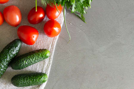 Fresh, delicious vegetables cucumbers, tomatoes and greens with dill and parsley lie on the kitchen, gray surface on a linen towel and are ready for cooking pasta or salad.の写真素材
