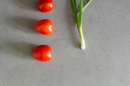 Fresh tomatoes and green onions plucked from the garden are on the gray, working surface of the kitchen. Tomatoes are laid out in a row and ready for cooking according to the recipe.の写真素材