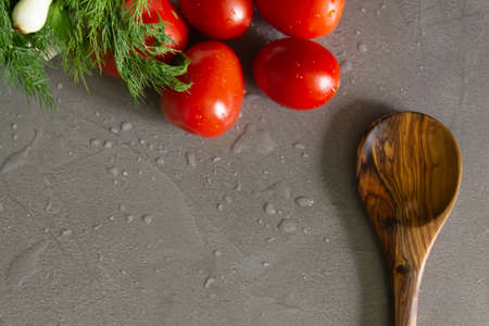 Bamboo spoon and fresh vegetables tomatoes, lettuce, dill and onions, green onions from the garden are washed with water and lie on the table with drops of water on the surface. beautiful background. Salad preparation in a restaurant according to the cook's recipe.の写真素材