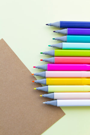 Multi-colored markers for sketching, for drawing drawings and objects, for working in the office and studying at school, with open caps and a sheet of craft paper on a light yellow background.の写真素材