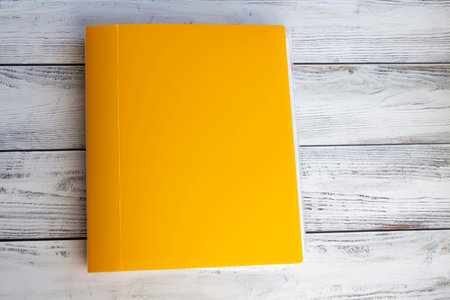 A bright, yellow, thick, stationery folder with a large number of documents for office work and university studies on a light, wooden background.の写真素材