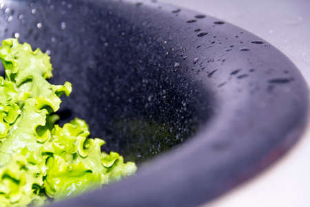 Green salad with drops of water in a black sink for the preparation of delicious dietary and vegatarian dishes.の写真素材