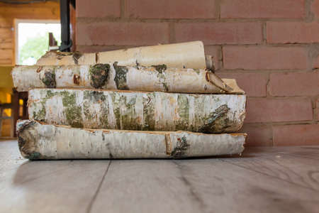 Birch firewood lies on the floor of a wooden house near the fireplace to heat the house on cold days..の写真素材