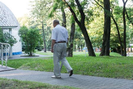 An old, stooped man walks sullenly and alone along the path in the park with a gray umbrella instead of a cane..の写真素材