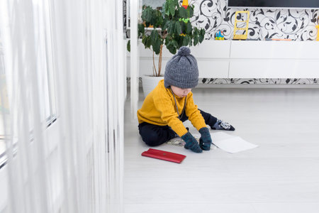 A little boy in a yellow sweater and hat is counting money and studying heating bills, near a heater with a thermostat..の写真素材
