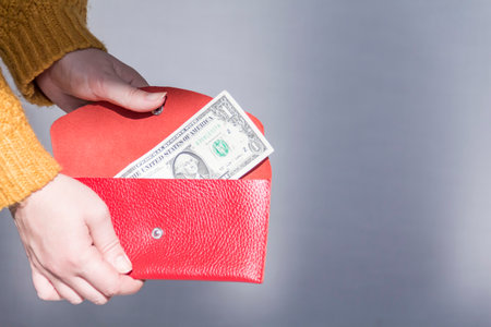 Women's hands in a yellow sweater are holding an open, red purse with money..の写真素材