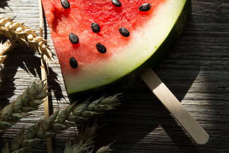 A piece of sweet watermelon on the ice cream shelf and ripe wheat ears on a wooden surface.,,の写真素材