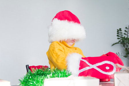 A cute little boy in a yellow sweater, a red Santa Claus hat and Christmas mittens with gifts in his hands. Celebrate Christmas and New Year.の写真素材