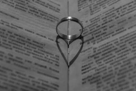Wedding ring with a falling shadow in the form of a heart standing on an open book.の写真素材