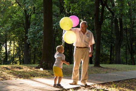 A little boy in yellow shorts and an elderly old man are playing with bright balloons. The family is having fun in the park in the fresh air and celebrating the holiday..の写真素材