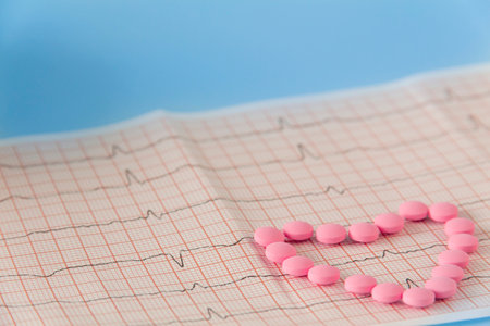 A large handful of pink pills lie in the form of a heart on an electrocardiogram, on a blue background. The concept of a healthy lifestyle and timely medical examinationの写真素材
