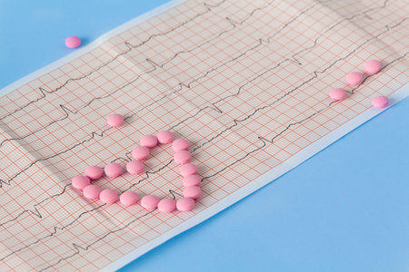 A large handful of pink pills lie in the form of a heart on an electrocardiogram, on a blue background. The concept of a healthy lifestyle and timely medical examinationの写真素材