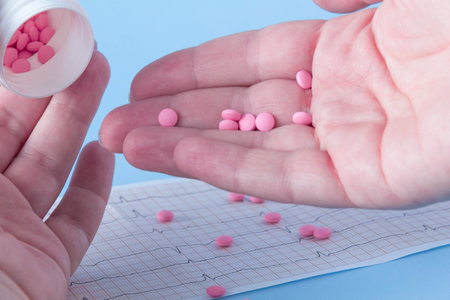 A hand pours a handful of pink pills from a white jar onto an electrocardiogram of the heart, on a blue background. The concept of a healthy lifestyle and timely medical examinationの写真素材