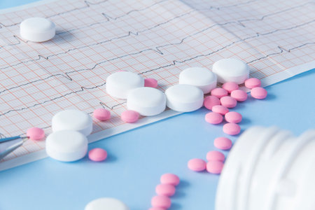 A large handful of pink and white medicines are spilled from a jar on a heart electrocardiogram, on a blue background. The concept of a healthy lifestyle and timely medical examinationの写真素材