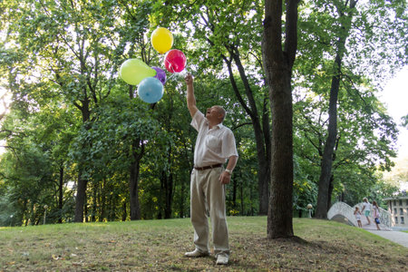 An old man is playing in the park with bright, balloons on his birthdayの写真素材