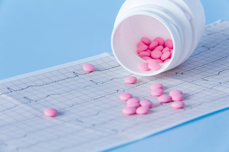 A large handful of pink pills poured out of a white jar on an electrocardiogram of the heart, on a blue background. The concept of a healthy lifestyle and timely medical examinationの写真素材