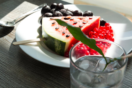Summer snack. Fresh berries and fruits on a wooden table with green leaves of plants.の写真素材