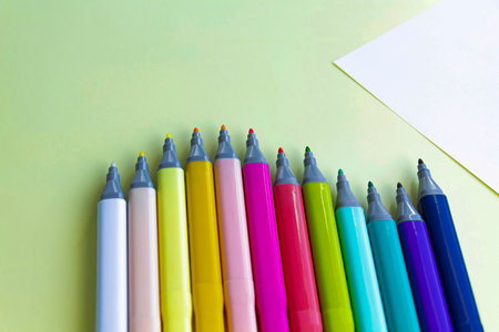 Multi-colored markers for sketching, for drawing drawings and objects, for working in the office and studying at school, with open caps and a white sheet of paper on a light yellow background.の写真素材