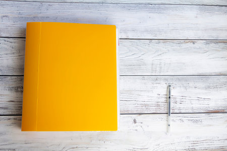 A bright, yellow, thick, stationery folder with a large number of documents and a ballpoint pen for office work and university studies on a light, wooden background.の写真素材