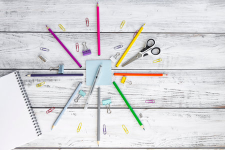 Bright, multicolored pencils for drawing in an album, colored paper clips, a blue notepad for notes, scissors, a pen, a metal sharpener and clips are folded neatly in a circle on wooden background.の写真素材