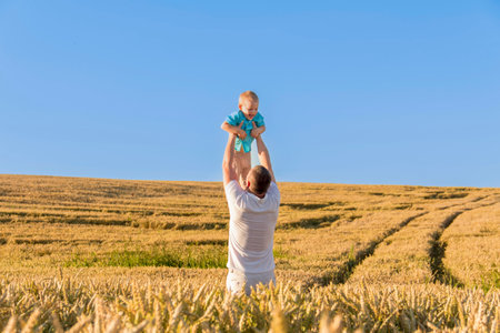 Dad and his little son are having fun walking in a field with ripe wheat. Grain for making bread. the concept of economic crisis and hungerの写真素材