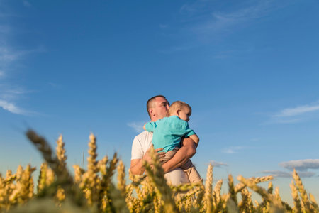Dad and his little son are having fun walking in a field with ripe wheat. Grain for making bread. the concept of economic crisis and hungerの写真素材
