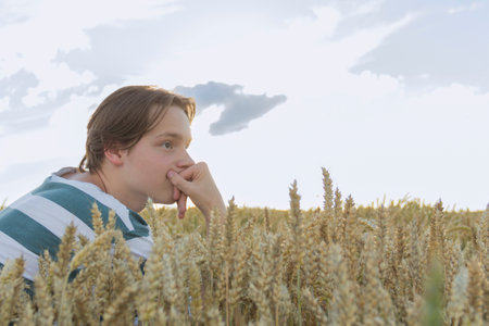 A young guy, a teenager with ears of ripe wheat in a farmer's field, against a blue sky. Grain for making bread. the concept of economic crisis and hungerの写真素材