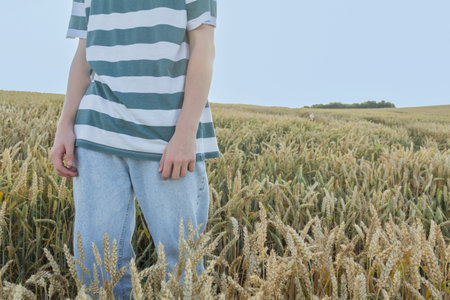 A young guy, a teenager with ears of ripe wheat in a farmer's field, against a blue sky. Grain for...