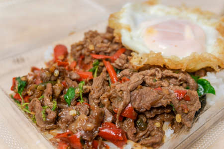 Close up Rice topped with stir-fried beef and holy basil with egg in a plastic box, popular Thai street food.の写真素材