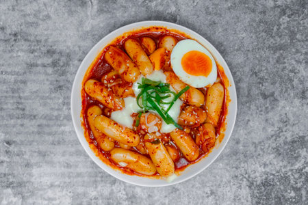 Top view Tteokbokki (Spicy Rice Cakes) with boiled eggs and cheese on the grey concrete table, Korean street food.の写真素材