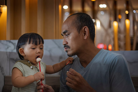 Father teaches toddler baby to eat meatball. Father and son are eating together in the restaurant.