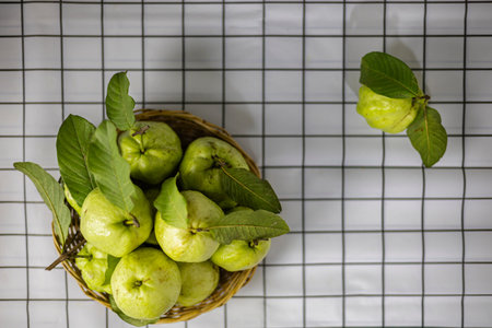 Green Guava In The Bamboo Basket On The Table, A cozy wooden table holds a bamboo basket with...