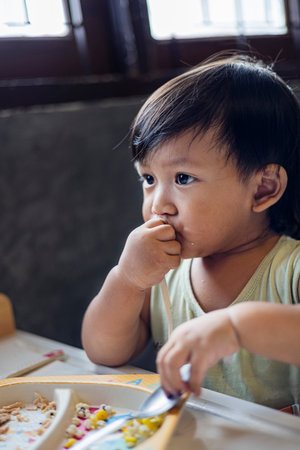 Toddler Is Eating Breakfast By Himself, A cute toddler enjoys breakfast by himself with a big smile, great for family lifestyle marketing images.の写真素材