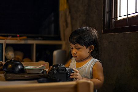 Toddler Exploring Photography Camera, A curious toddler fiddles with a photography camera, tiny fingers on lenses in soft light, perfect for a family photography shot or a playful discovery showcase.の写真素材
