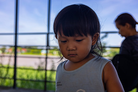 Toddler Sits Waiting For His Mother Who Is Playing On Phone, A patient toddler sits waiting, gazing at his mother engrossed in her phone.の写真素材