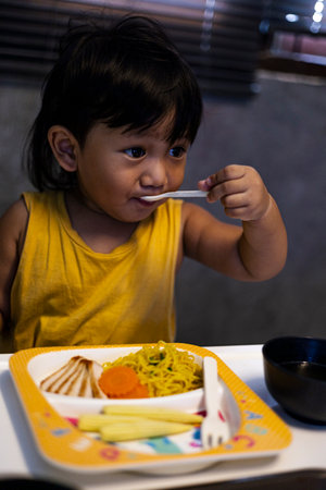 Toddler Is Eating Noodles With Soup, A warm photo of a toddler eating noodles with soup, steam rising in soft light, perfect for a family dining campaign or a cozy mealtime documentary.の写真素材