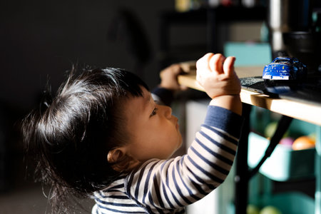 Toddler Standing To Reach Toy On Table, A cute photo of a toddler on tiptoes reaching a toy on the...