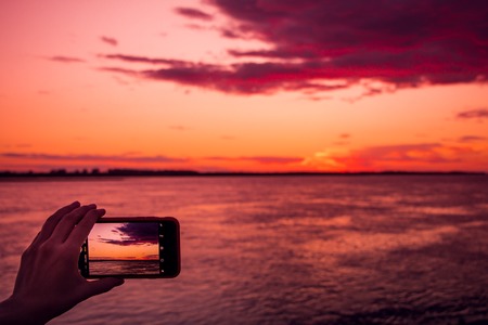 shooting the pink sunset with beautiful clouds over a river on a smartphoneの写真素材